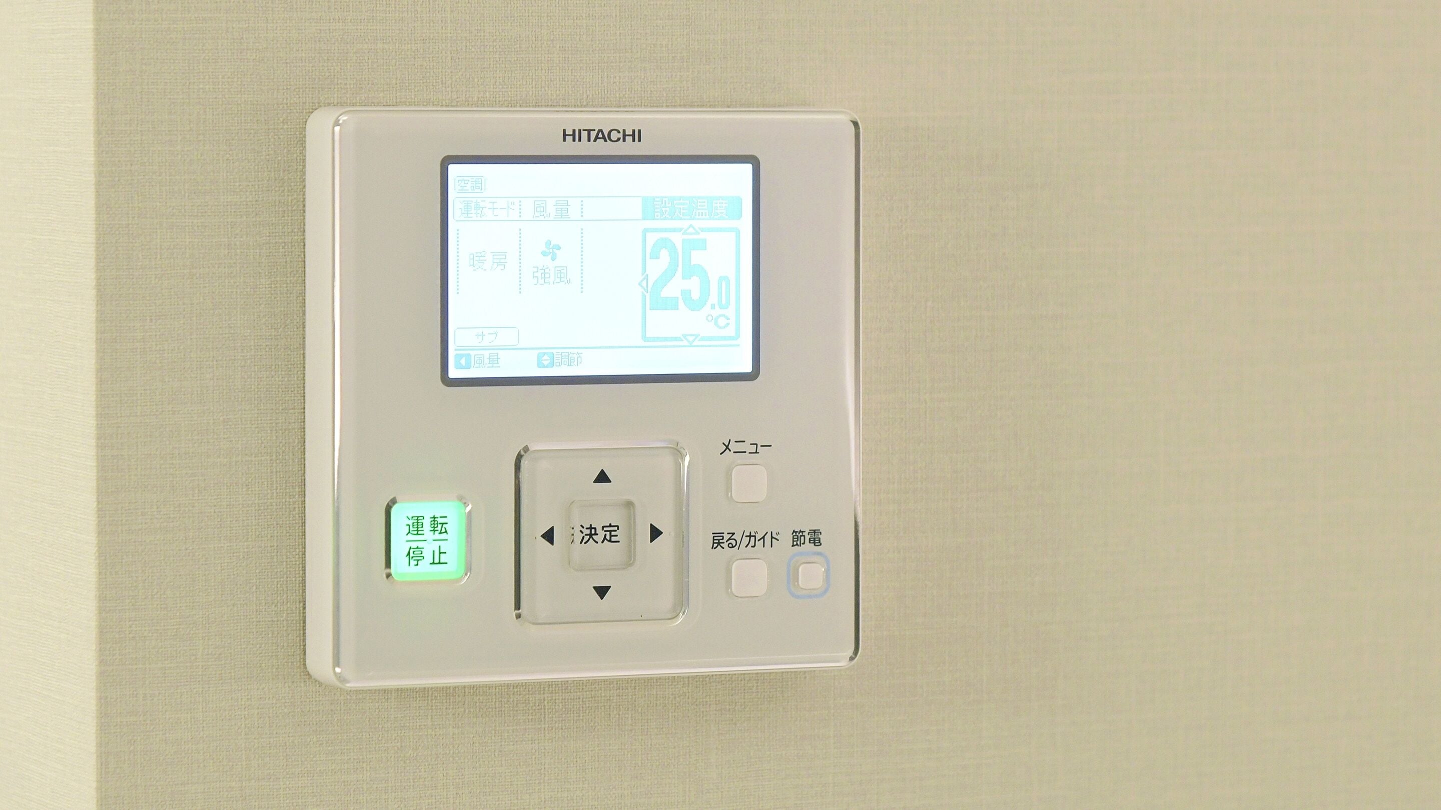 A HITACHI air conditioning unit with a digital display, a remote control, and a power button.