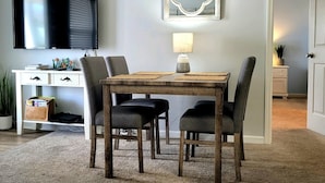 Un comedor con una mesa de madera, cuatro sillas, un televisor sobre la mesa, un espejo decorativo y una lámpara en la mesa.