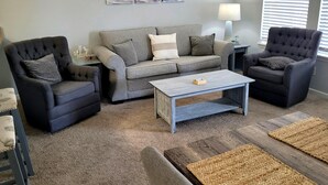 Una sala de estar con un sofá gris, dos sillones, una mesita de centro y una lámpara.