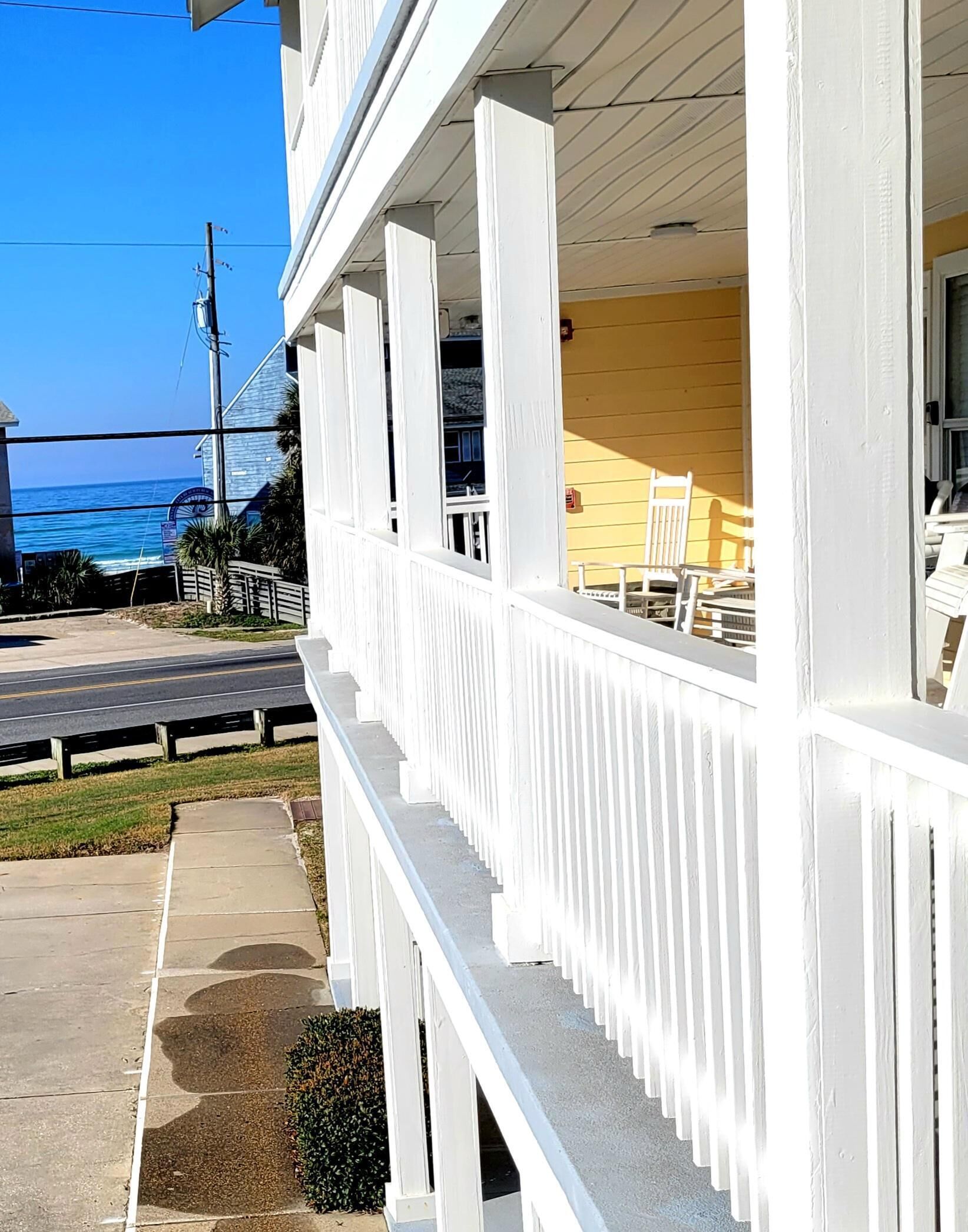 A white building with a balcony overlooking a road and a view of the ocean.