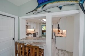 A kitchen with a marble countertop, wooden chairs, and white cabinets.