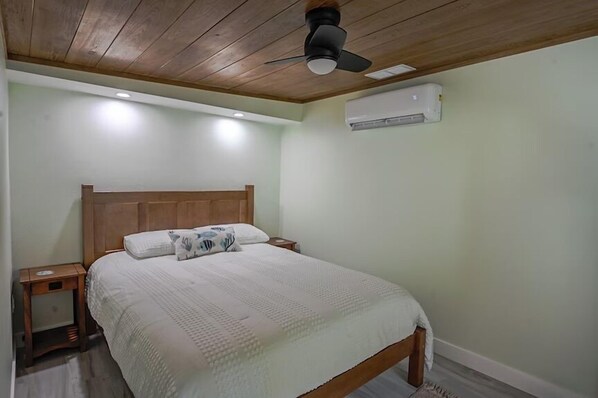 A bedroom with a wooden bed, bedside tables, a ceiling fan, and an air conditioning unit.