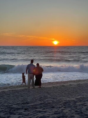 A sunset over the ocean with a family and a dog on a beach.