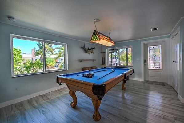 A pool table in a room with large windows and a door leading outside.