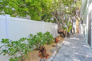 A narrow pathway flanked by a white fence and various plants, leading to a building with a garage.