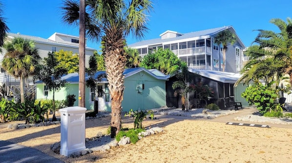 Una propiedad frente a la playa con una casa grande, un edificio más pequeño y una zona arenosa con palmeras.