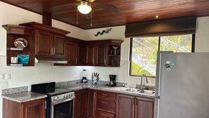 A kitchen with wooden cabinets, a stainless steel refrigerator, a built-in oven, and a window with a view of greenery.