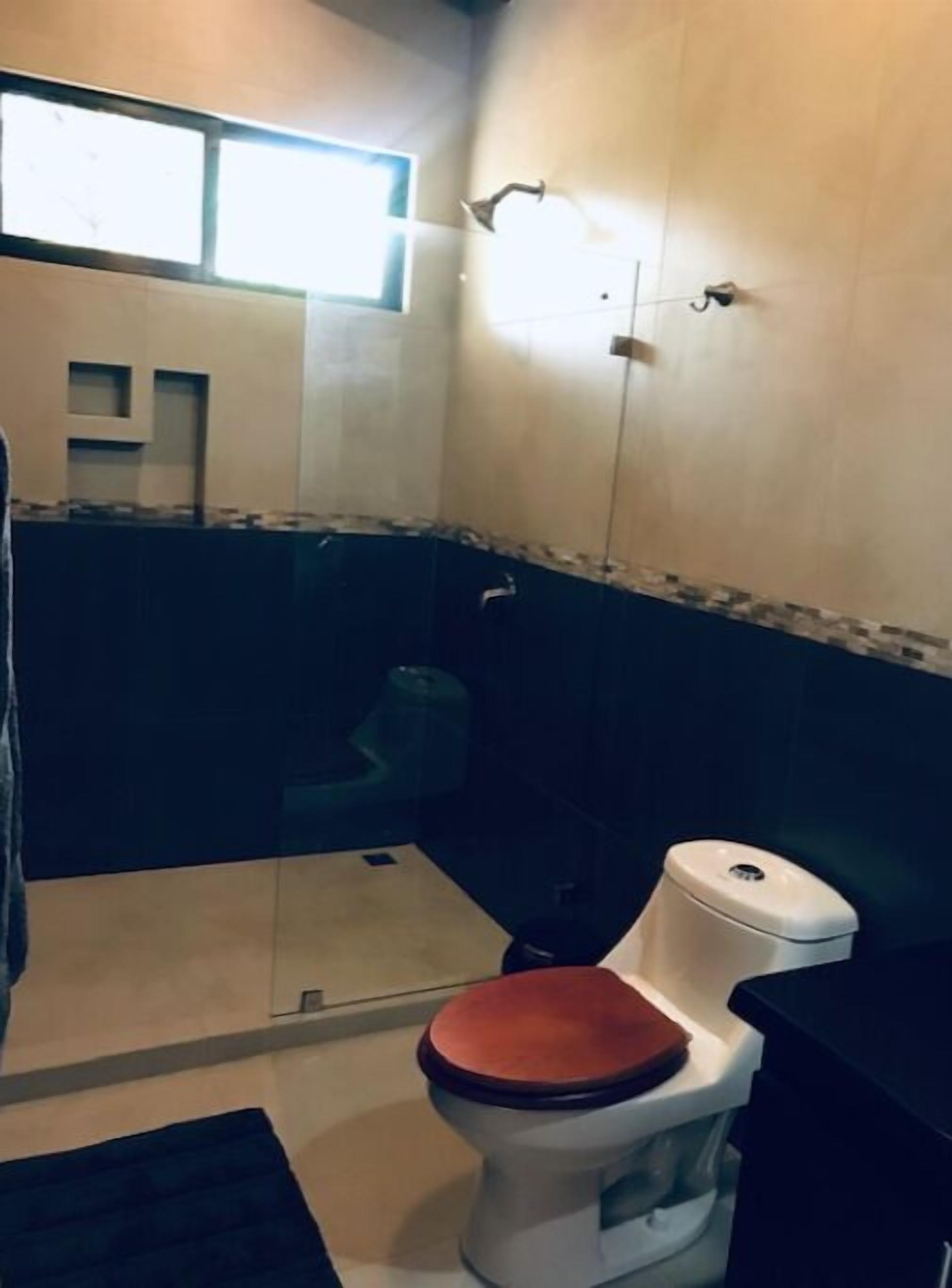 A small bathroom with a toilet, a shower, and a window.