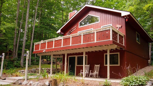 Une cabane rouge dotée d’un balcon, entourée d’une forêt.