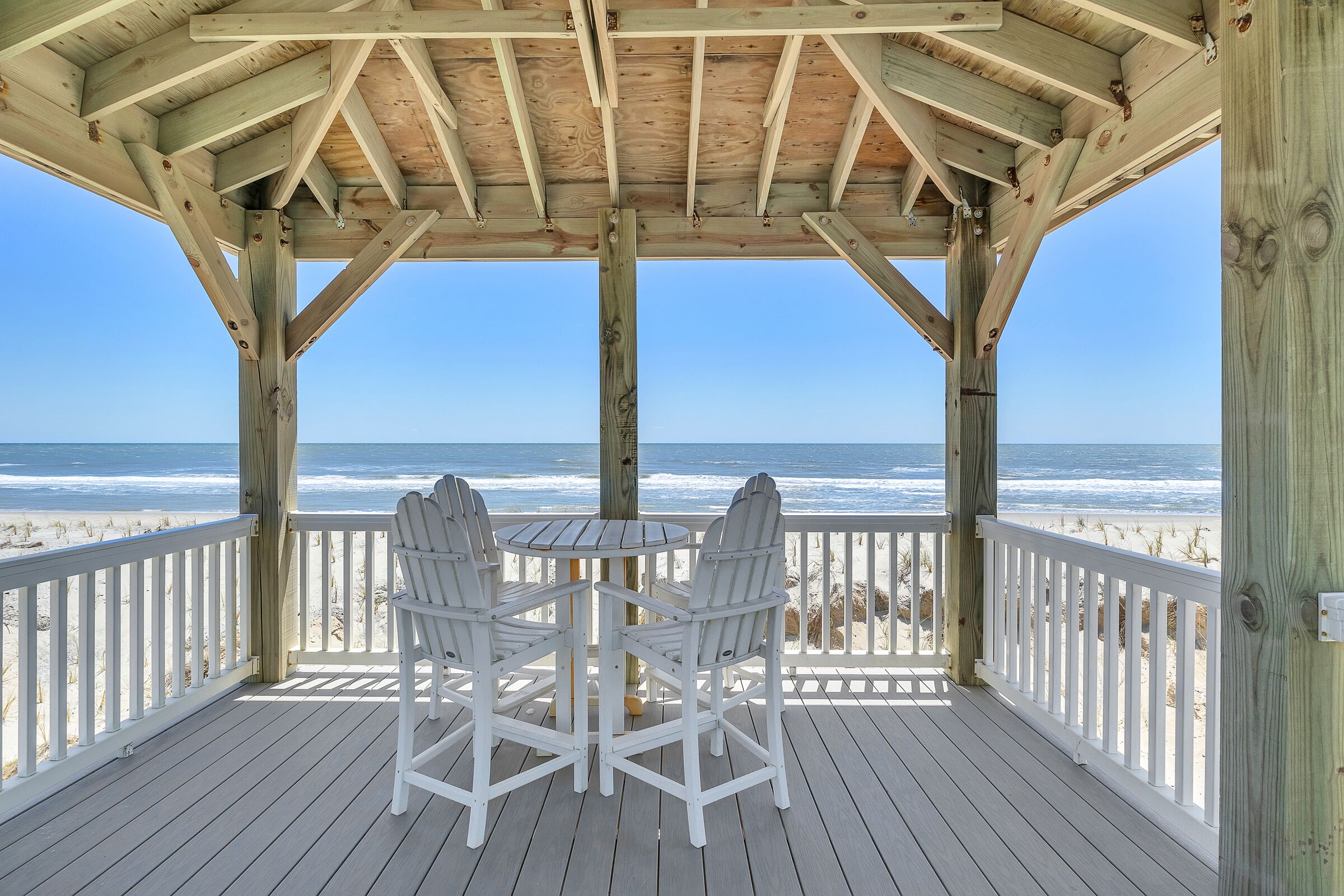 A wooden deck with a table and chairs overlooking the beach.