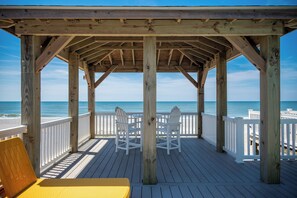 A wooden deck with white railings, two white chairs, and a yellow chair.