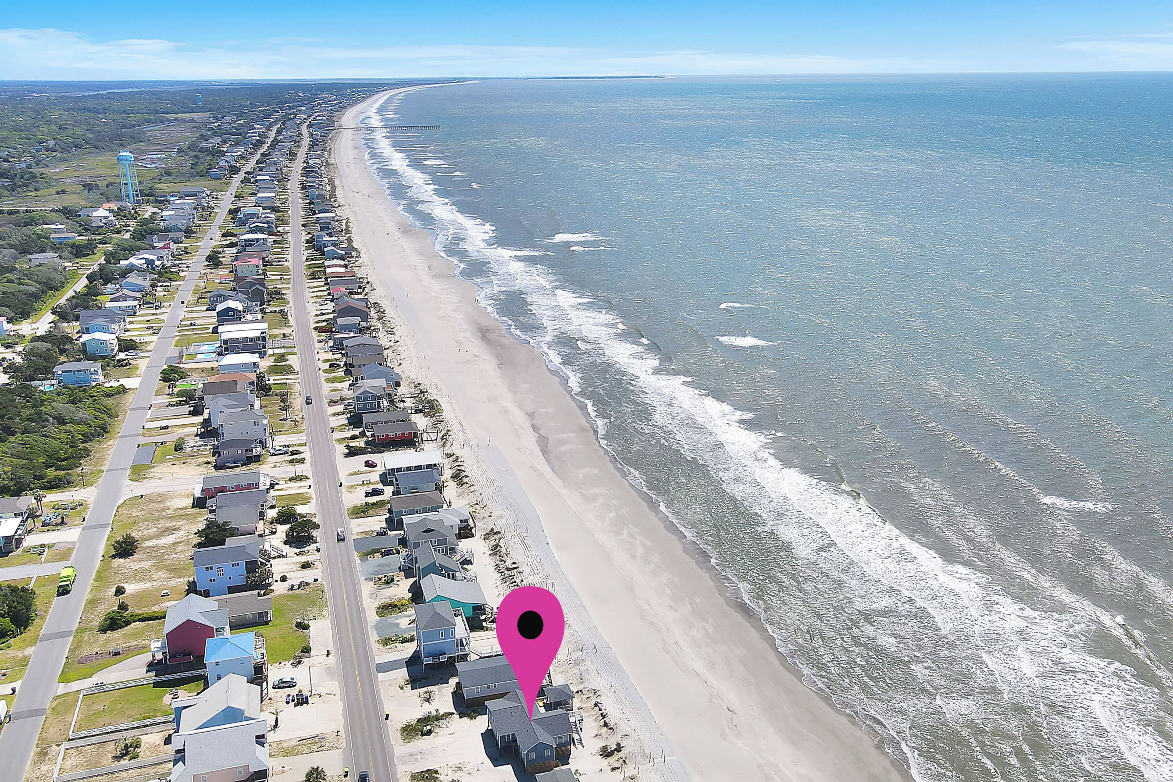 Vista aerea di una zona residenziale costiera con case disposte lungo la spiaggia, un cielo sereno e un mare calmo.