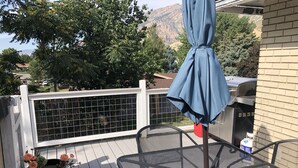 A patio with a metal table and chairs, a blue umbrella, and a white fence.