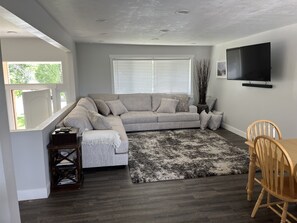 A living room with a grey sectional sofa, a black and white rug, a wooden dining table with chairs, and a TV mounted on the wall. - Ski Headquarters. Super clean. Sleep like a baby. (Cottonwood Heights)