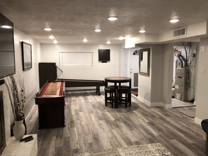A room with a pool table, a small round table with stools, and a decorative vase with branches.
