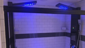 A bathroom with a shower enclosure, tiled walls, and a control panel with buttons and a digital display.