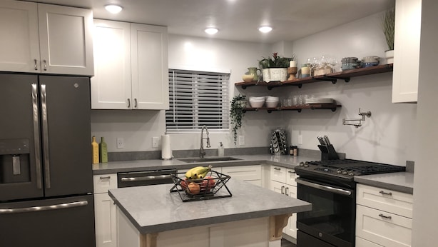 A modern kitchen with white cabinets, stainless steel appliances, a central island with stools, and a window with blinds.