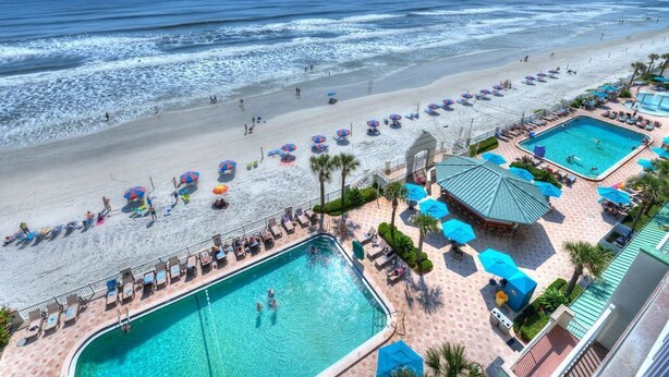 A beach resort with a swimming pool, beach umbrellas, and lounge chairs.