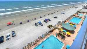 A beach resort with a swimming pool, beach umbrellas, and a view of the ocean.