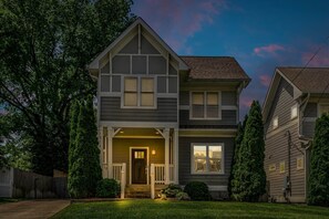 Une maison à deux étages avec un porche à l’avant, un garage et une pelouse bien entretenue.