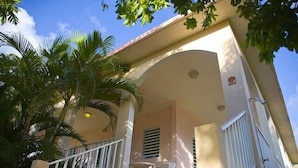 Edifici amb una zona exterior coberta, una barana blanca i una palmera.