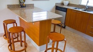 Cuina amb taulell de granat, tamborets de fusta, rentavaixelles i una finestra amb persianes.