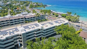 Een modern gebouw met meerdere verdiepingen, zonnepanelen op het dak en uitzicht op de oceaan en het strand.