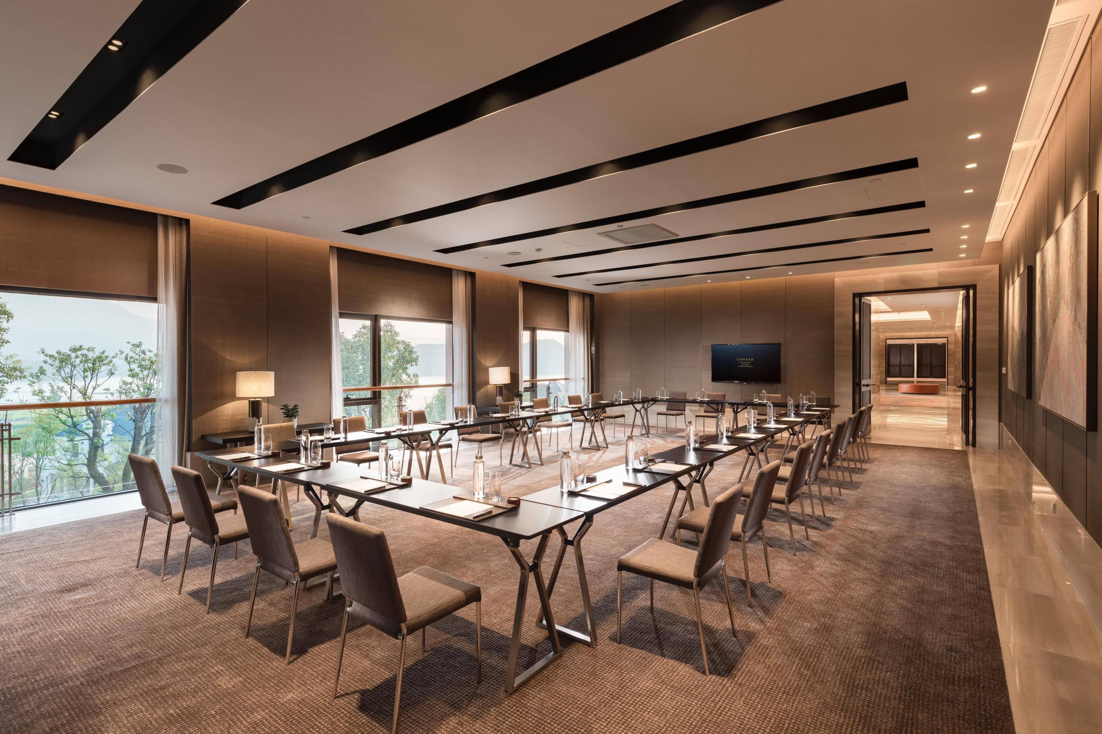 A conference room with a long table, chairs, a TV, and large windows.