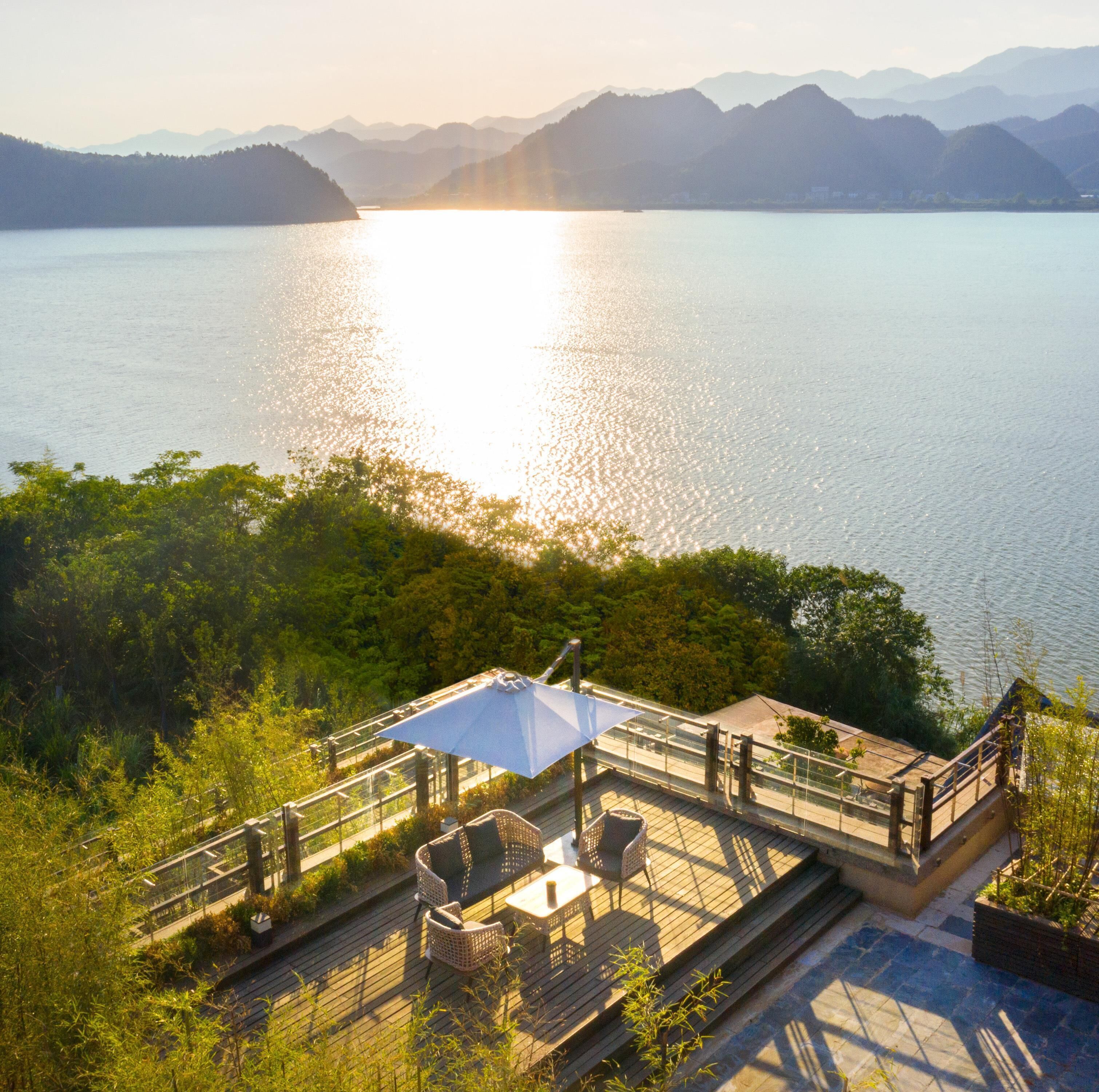 Une terrasse avec des sièges extérieurs donnant sur un lac, avec des montagnes visibles au loin.