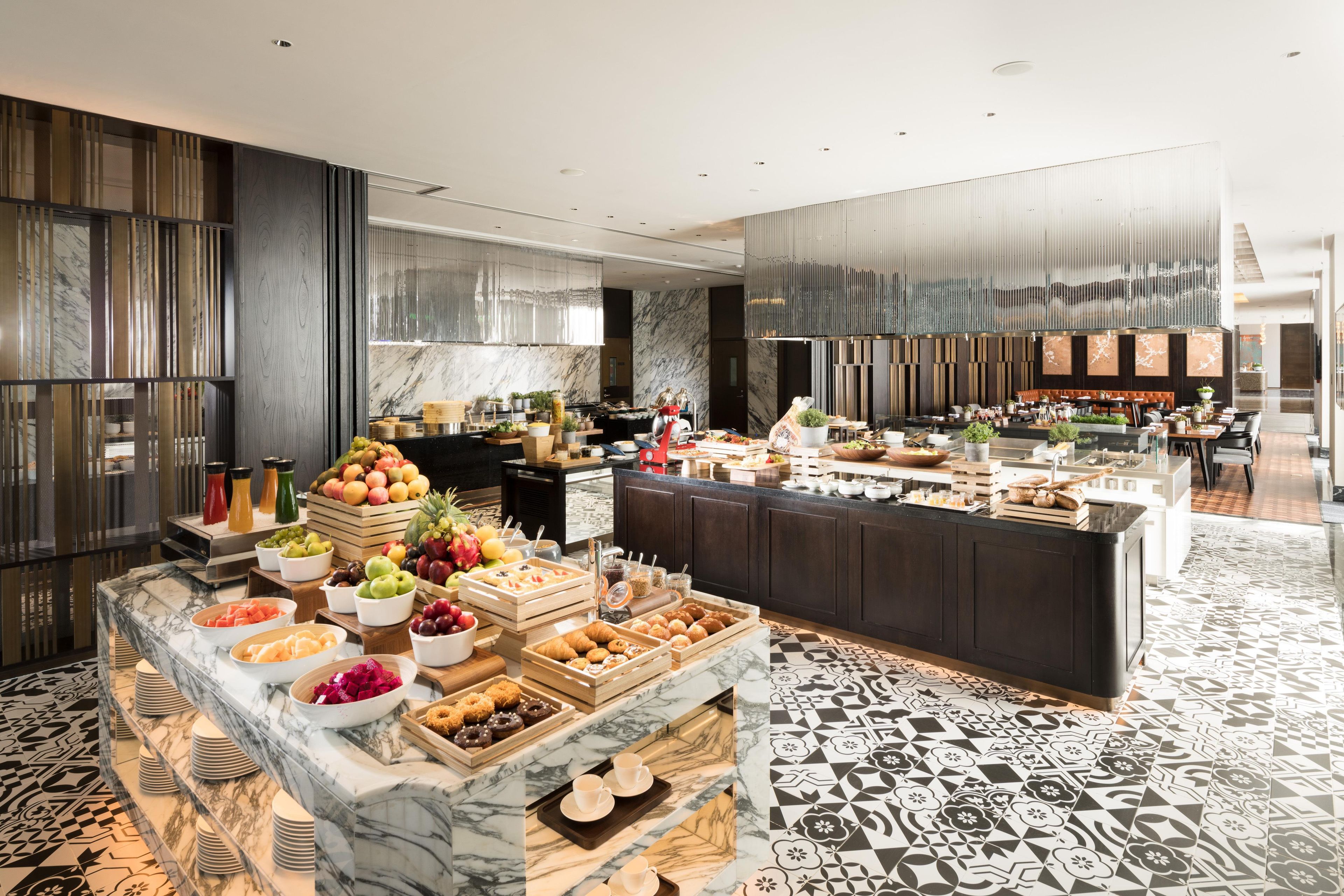 A modern kitchen with marble countertops, a central island with food and drinks, and a patterned floor.