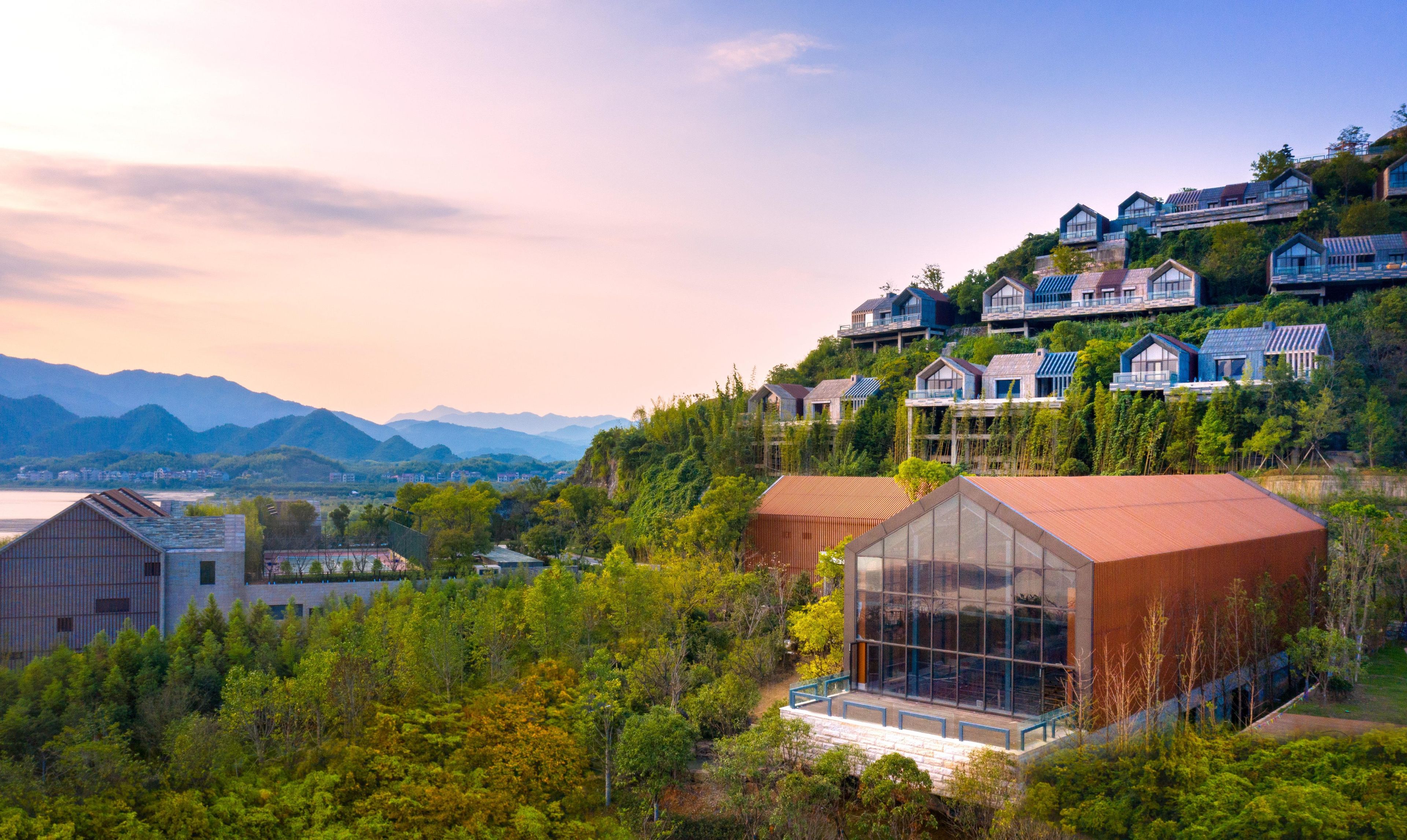 Una zona residencial moderna con casas en una ladera, un gran edificio de vidrio y montañas al fondo.