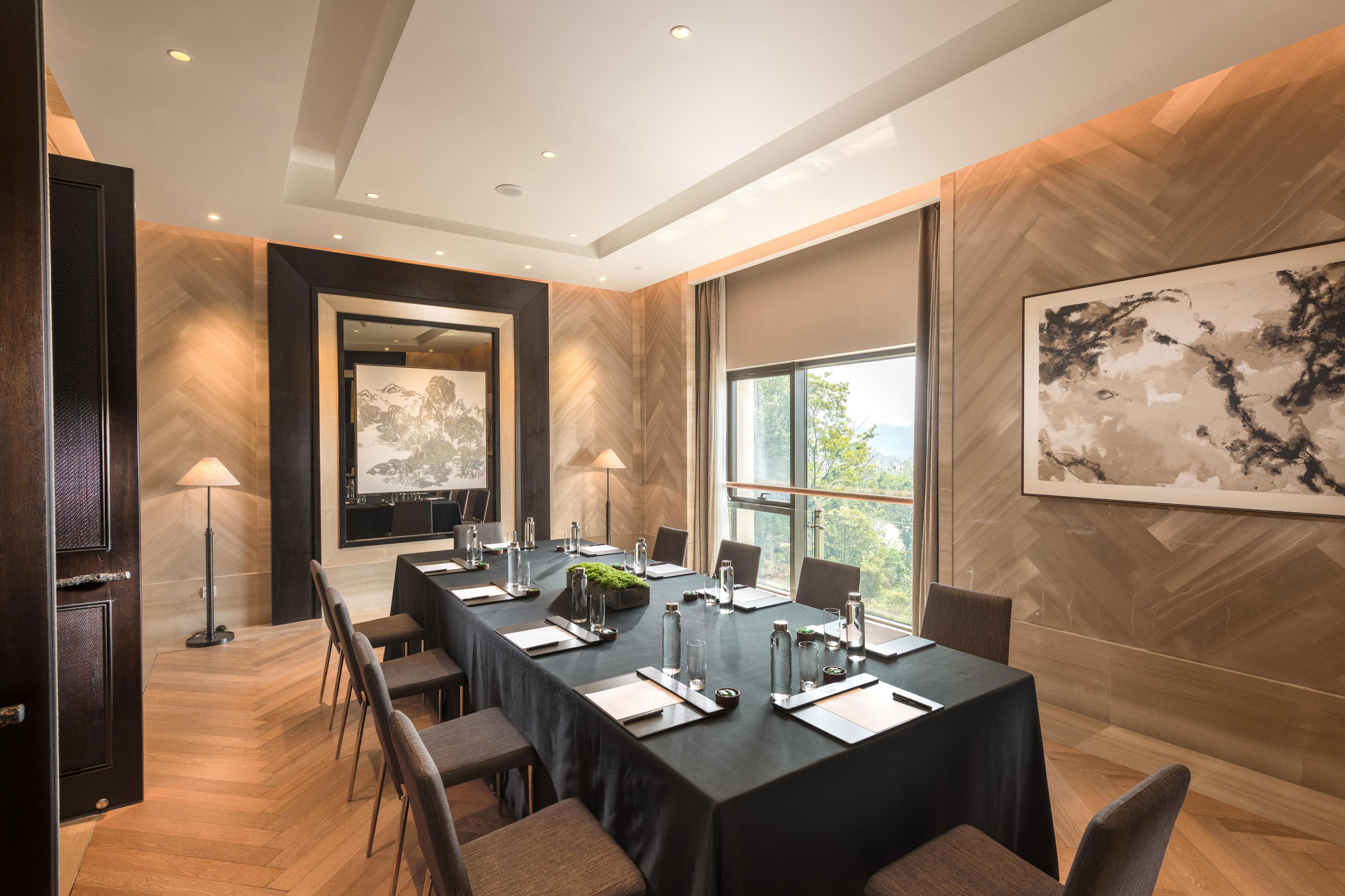 A conference room with a long table, chairs, a lamp, and a large abstract painting on the wall.