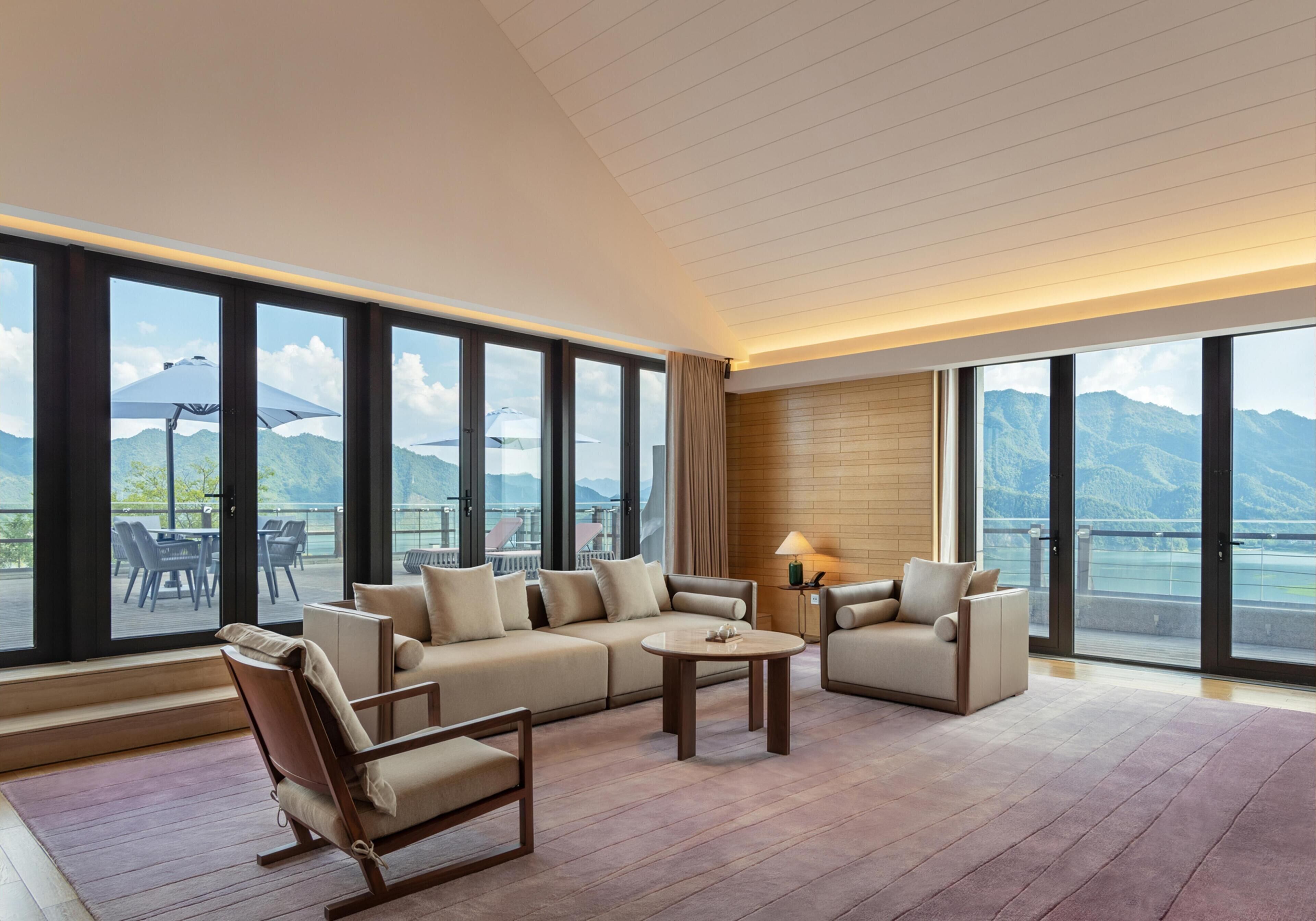 Amplia habitación con un sofá grande, sillones y una mesa de centro, que cuenta con un balcón con vista a la montaña.