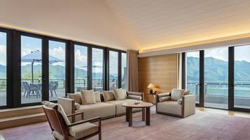 Amplia habitación con un sofá grande, sillones y una mesa de centro, que cuenta con un balcón con vista a la montaña.
