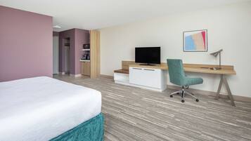A hotel room with a bed, a desk, a chair, a television, and a painting on the wall.