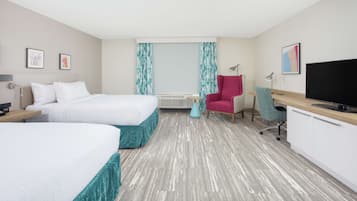 A hotel room with two beds, a desk, a chair, a TV, and a window with curtains.