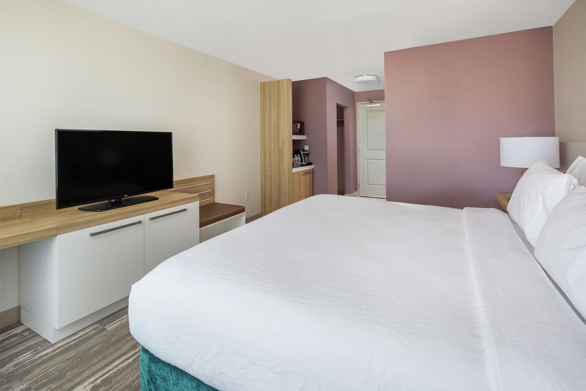 Et hotelværelse med seng, fjernsyn, skrivebord og garderobeskab.
