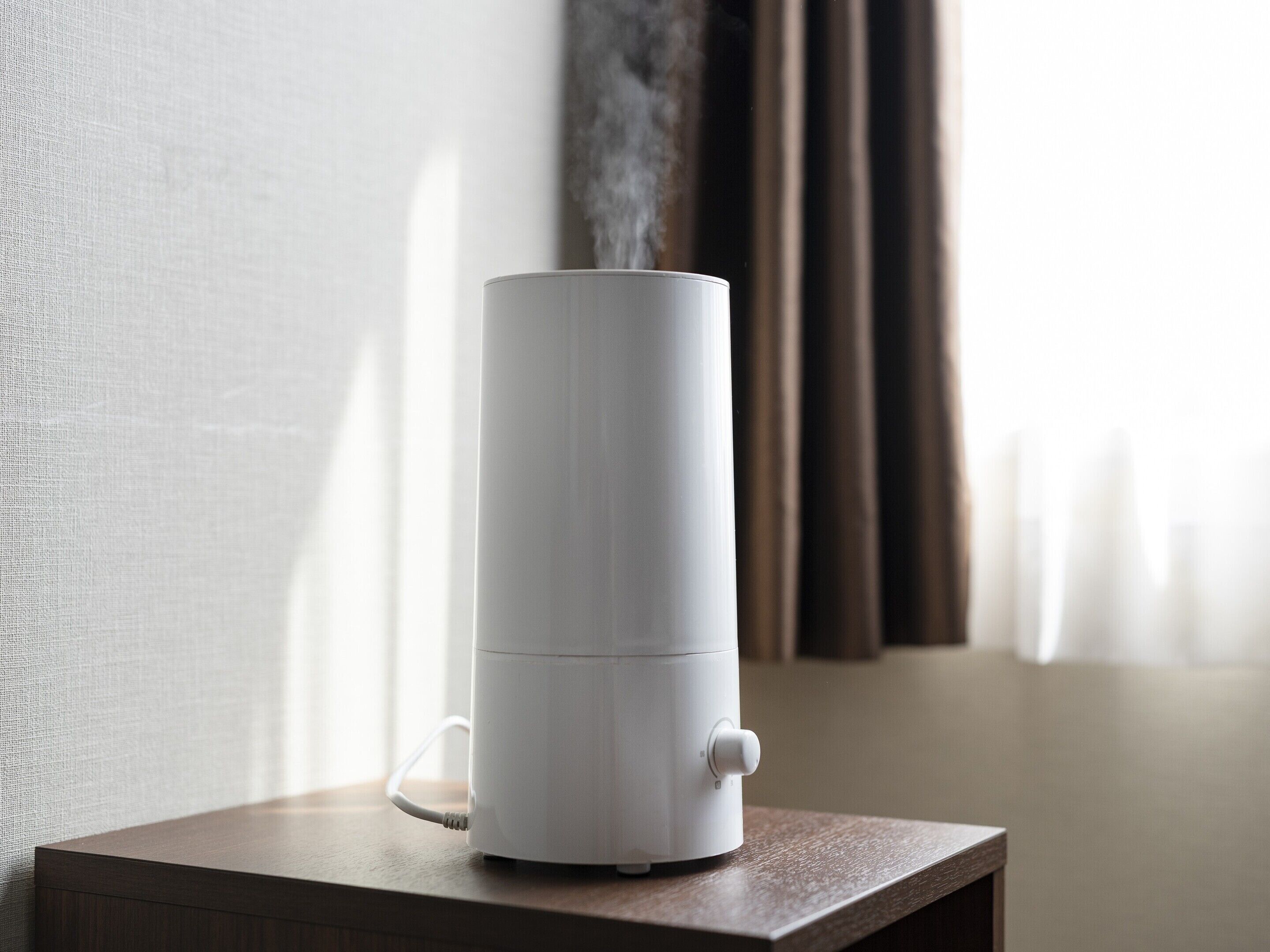 A white electric kettle on a wooden table near a window with curtains.