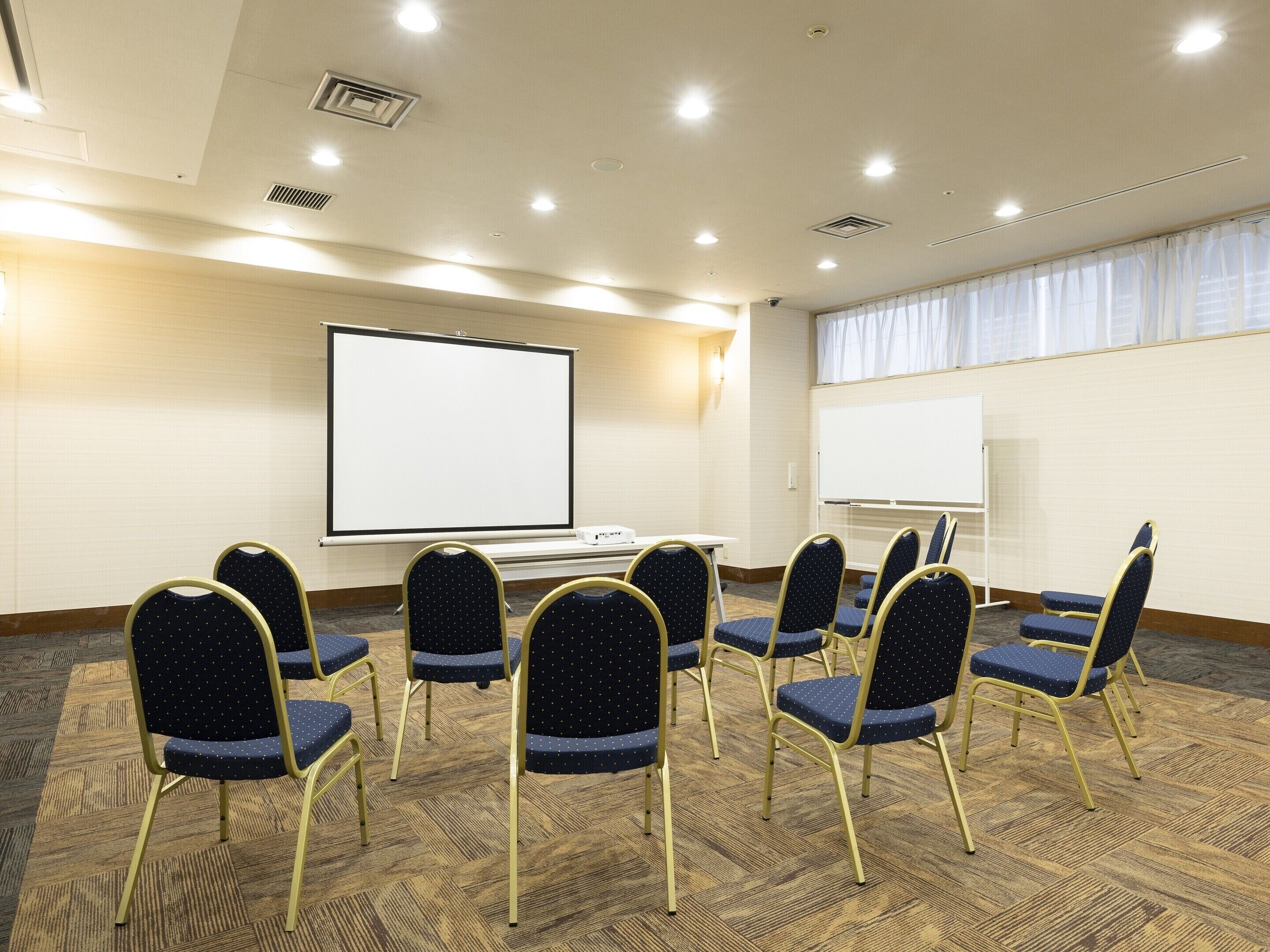 A conference room with a large screen, multiple chairs, and a carpeted floor.