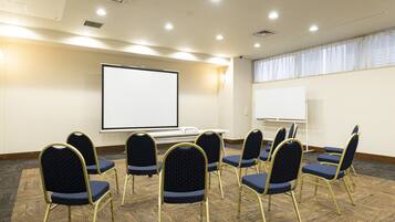 A conference room with a large screen, multiple chairs, and a carpeted floor.