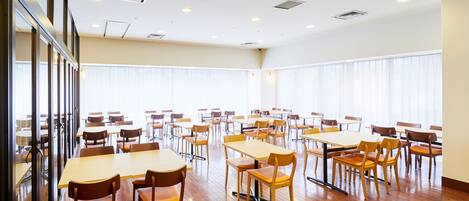 A spacious room with multiple tables and chairs, large windows, and a wooden floor.