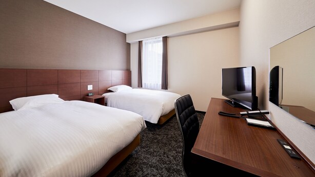 Una habitación de hotel con dos camas, un escritorio y una televisión, además de un espejo grande.