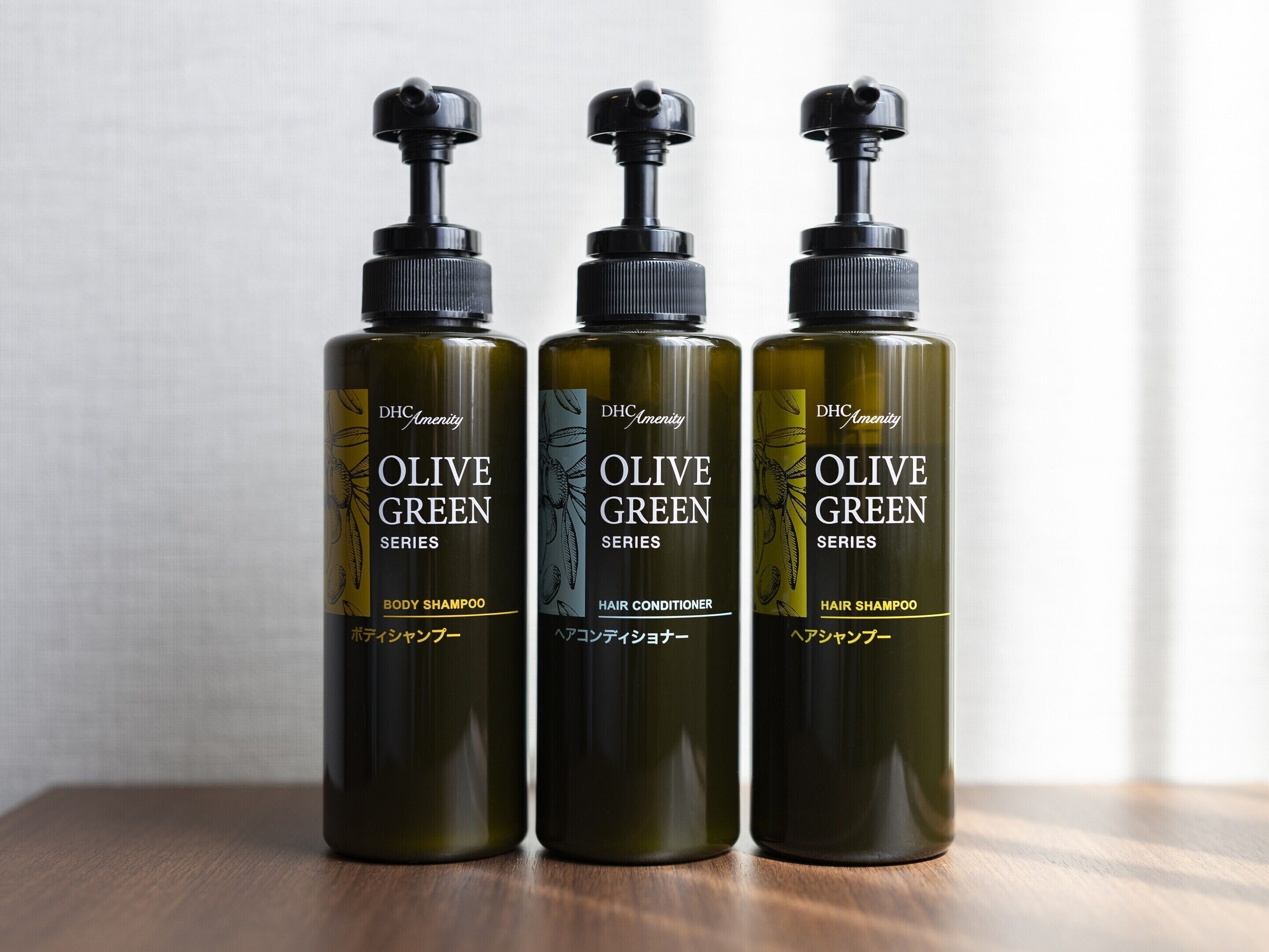 Three bottles of olive green hair care products on a wooden surface.