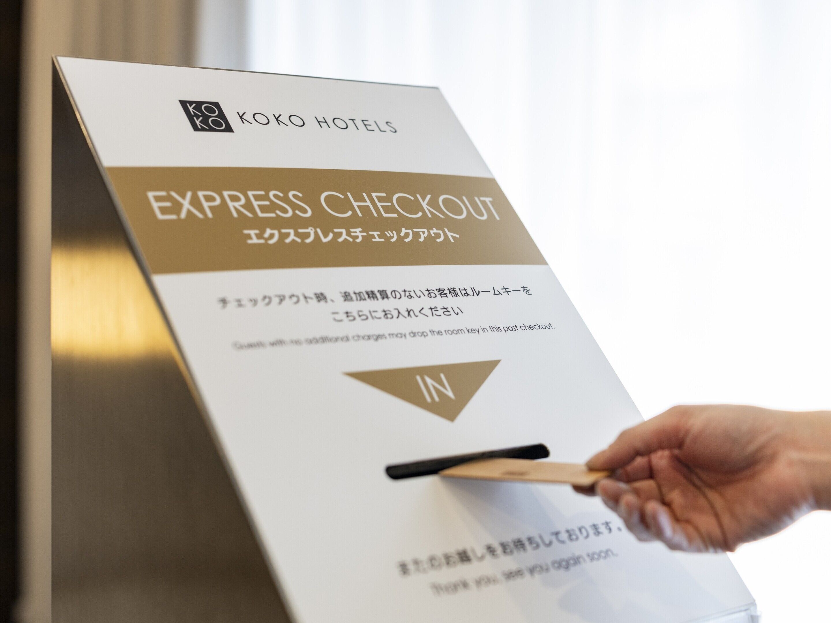 A hand inserting a key into a hotel room key card labeled 'EXPRESS CHECKOUT' with instructions in Japanese.