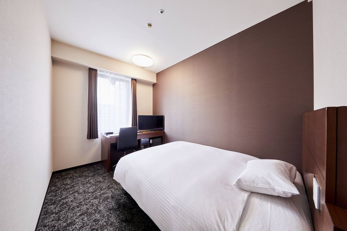 A hotel room with a bed, a desk, a chair, a television, and a window with curtains.