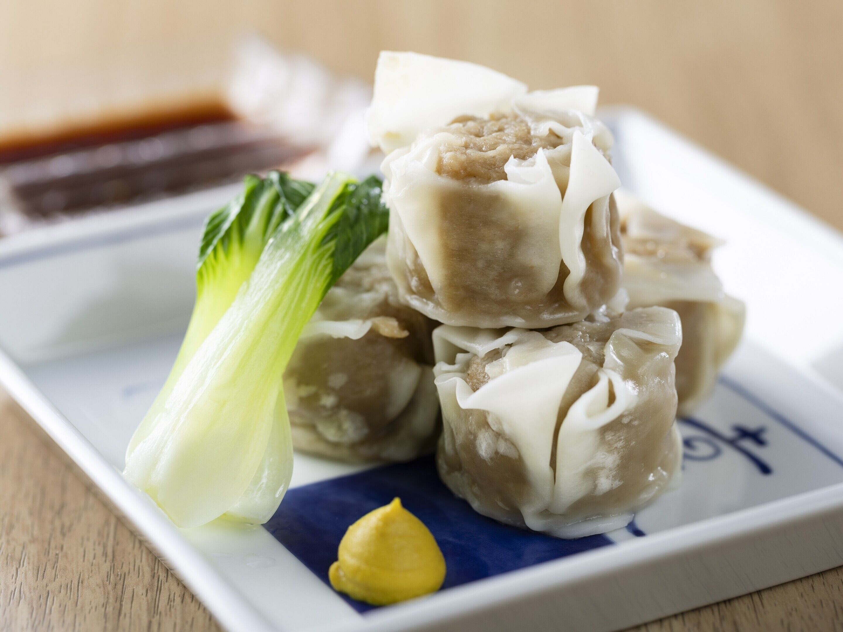 A plate of dumplings with a side of bok choy and a dollop of sauce.