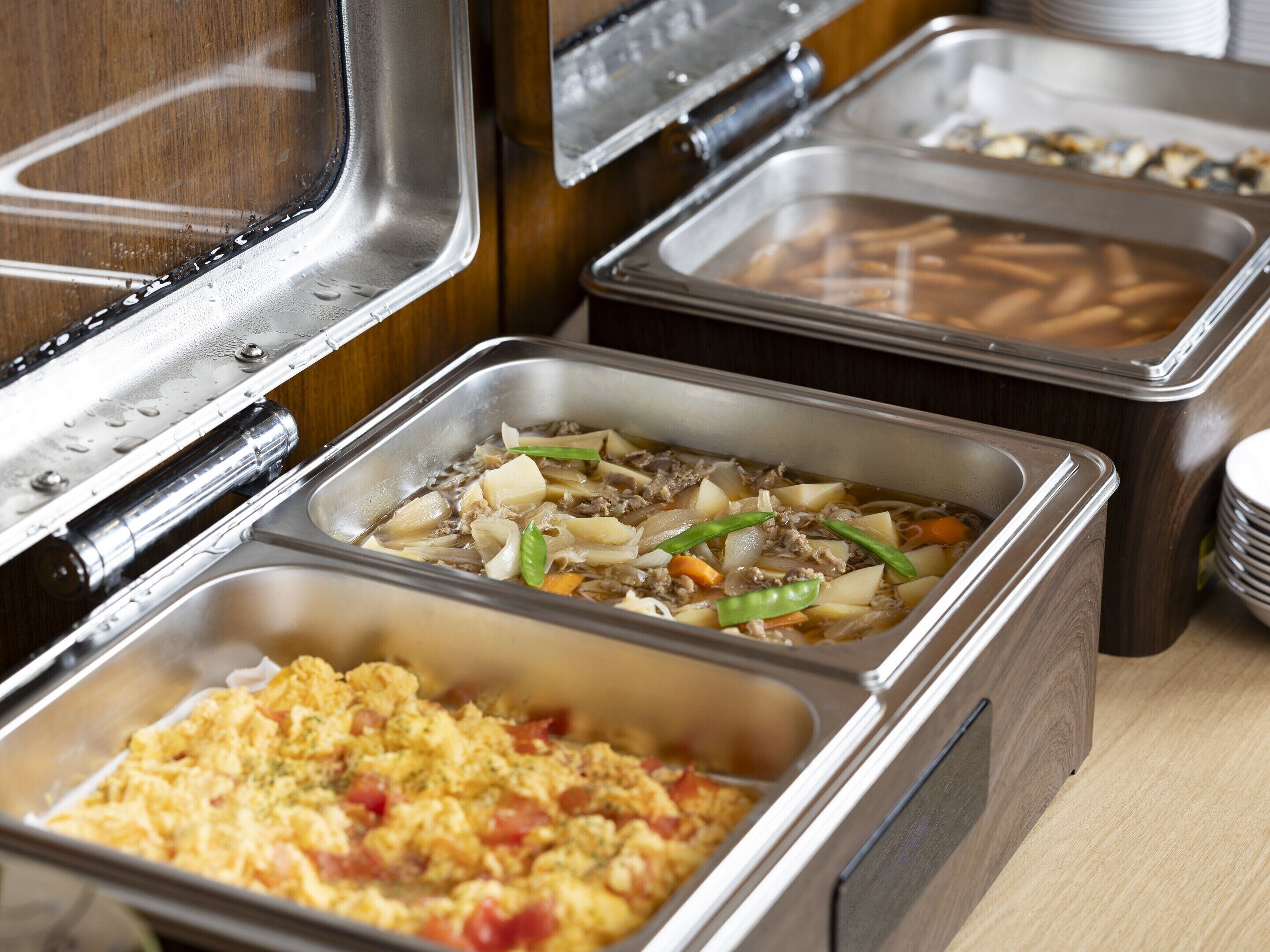 A buffet with various food options including scrambled eggs, a meat dish with vegetables, and a tray of what appears to be fried items.