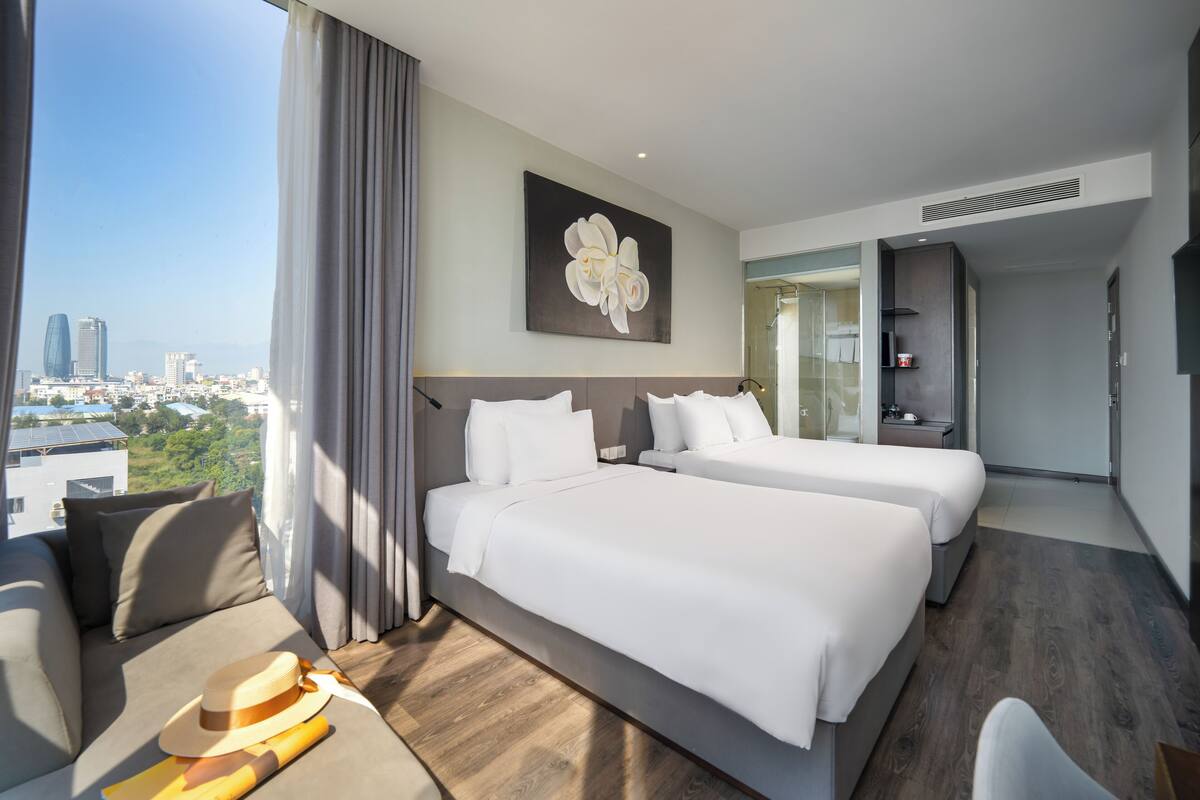 A hotel room with two beds, a sofa, and a city view.