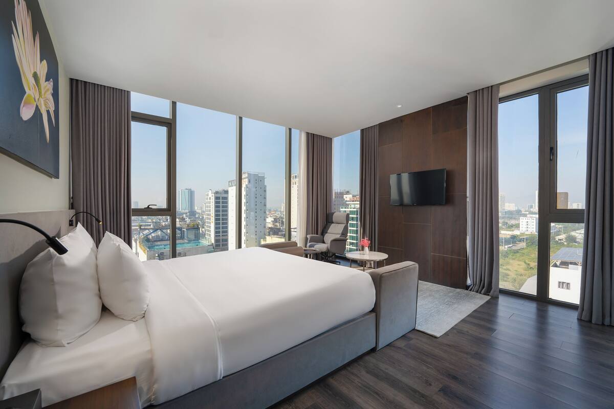 A modern hotel room with a large bed, a TV, and a city view.