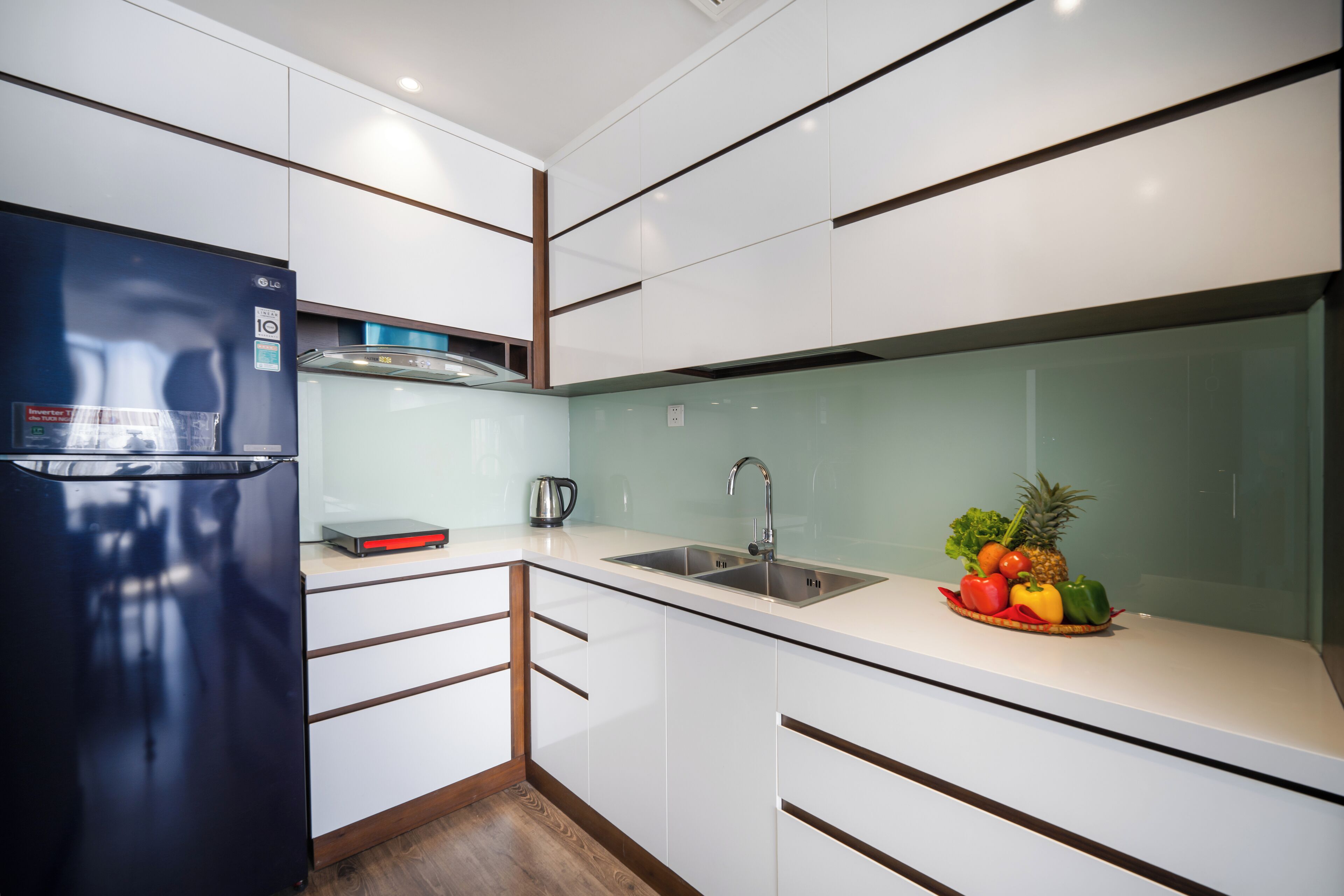 A modern kitchen with white cabinets, a black refrigerator, a stainless steel sink, and a fruit bowl on the counter.